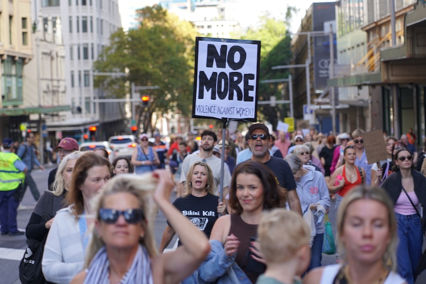 a gorup of people marching, a woman holds up a sign that says no more