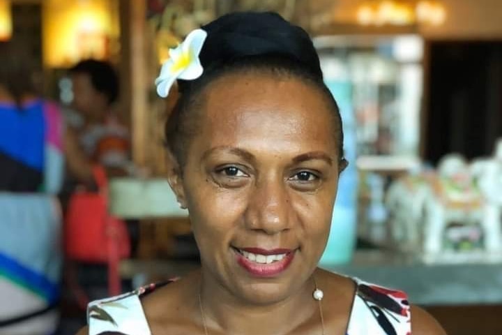 A woman wearing a floral white blue and pink dress with a frangipani behind her ear 