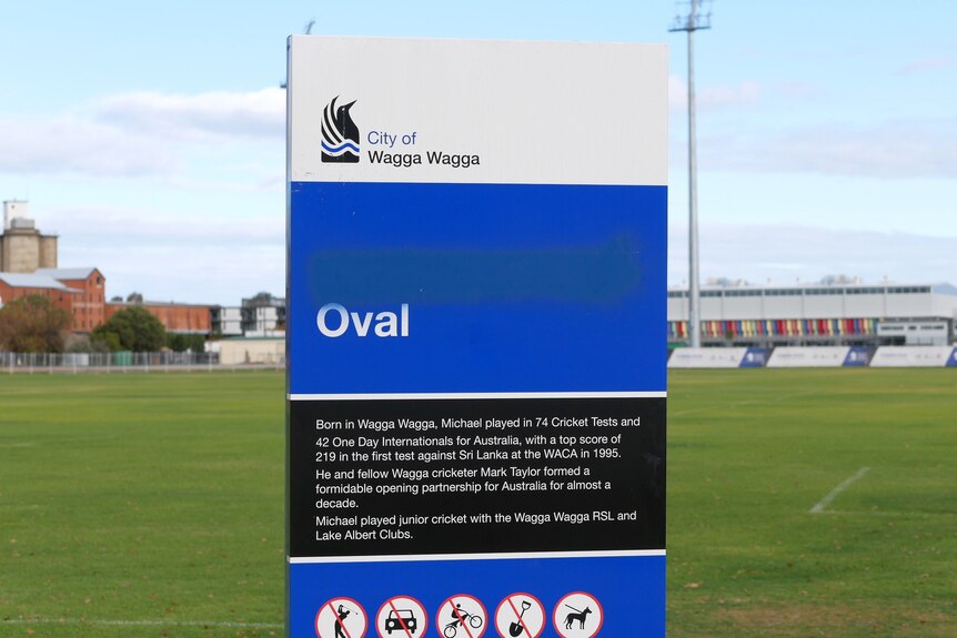 a blue, black and white sign in the middle of a sporting field.