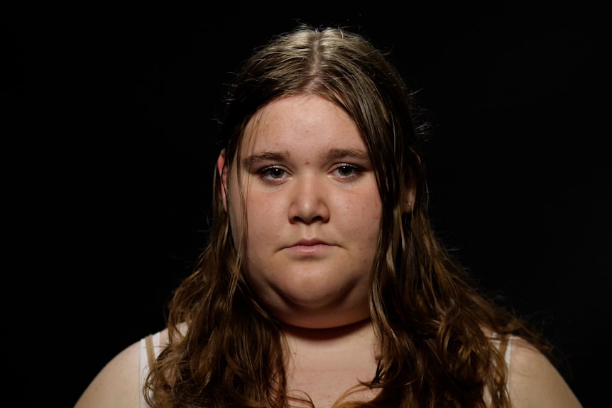 A young woman with light brown hair looking at camera. Black background.