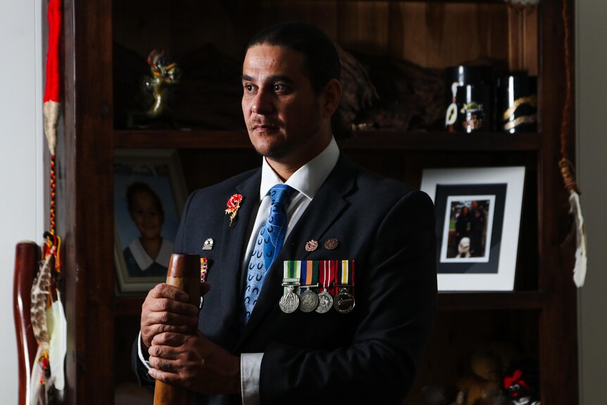 A man in a suit with military medals holding a didgeridoo.