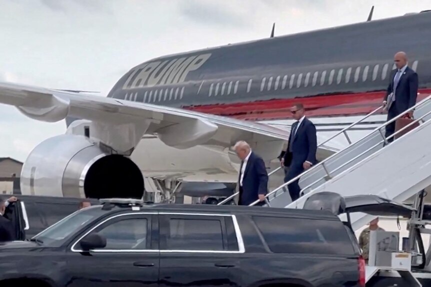 Donald Trump walks down stairs at the back of his plane.