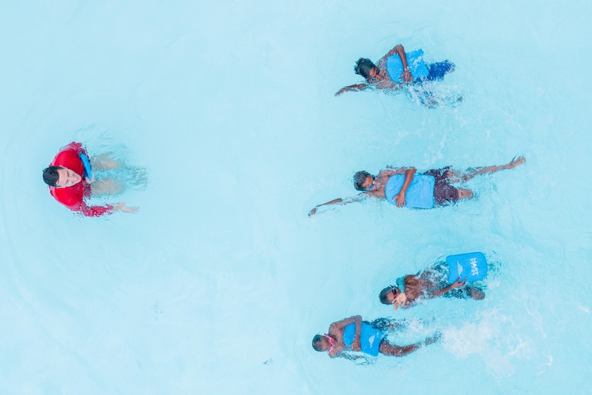 An aerial view of four children swimming backstroke in a clear blue pool