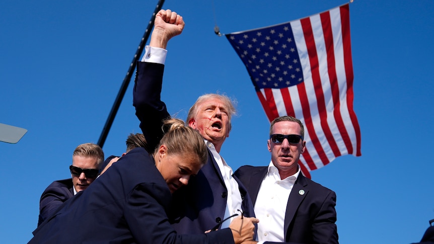 Donald Trump raises his fist while surrounded by secret service agents.