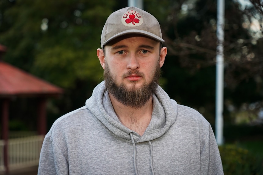 A man in a grey hoodie and cap looks at the camera.