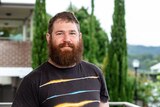 A man with a large beard smiling outside his home