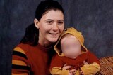 Young smiling woman with long dark hair pulled back, holding a baby, whose face is blurred.