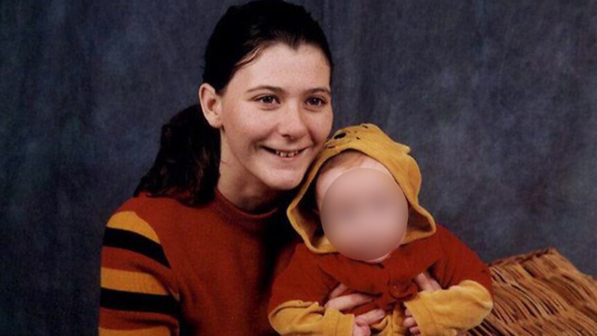 Young smiling woman with long dark hair pulled back, holding a baby, whose face is blurred.