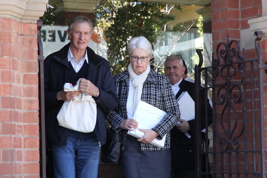 A grey haired man and woman leave a court house