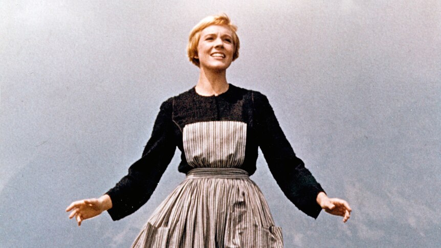 A young Julie Andrews in the sound of music standing on a foggy hill with her arms outstretched.