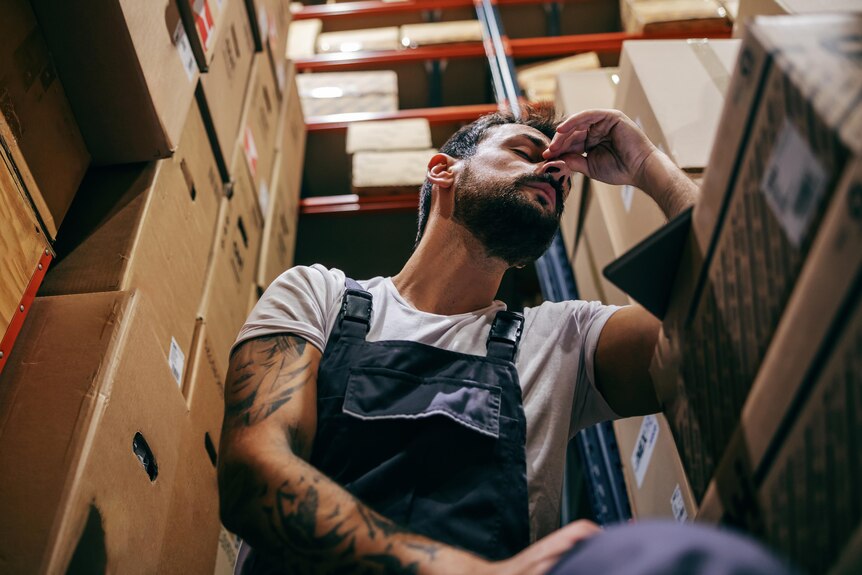 man sits in store room surrounded by boxes looking stressed