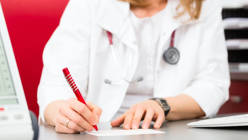 A female doctor wearing a stethoscope fills out a medical certificate