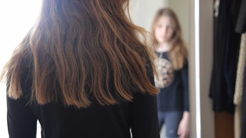 A female child stands in front of a mirror looking at their own reflection 