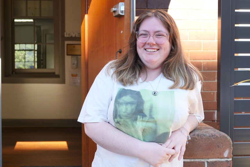 A woman stands in front of a school smiling. 