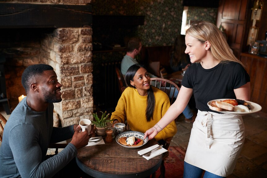 Waitress holding freshly cooked meals serves them to a table with a smiling couple.