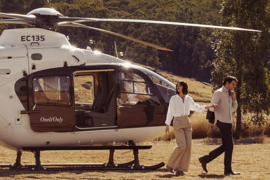 helicopter in paddock with man and women in front.