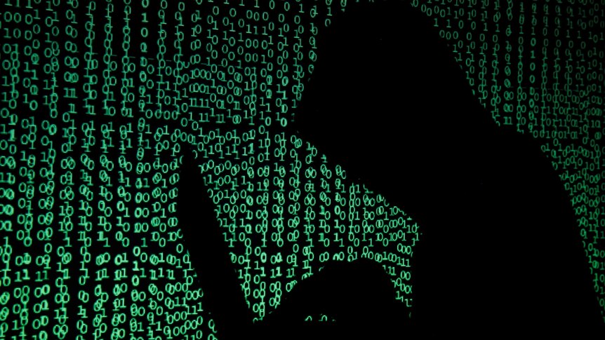 A hooded man holds a laptop computer as cyber code is projected on him in this illustration picture