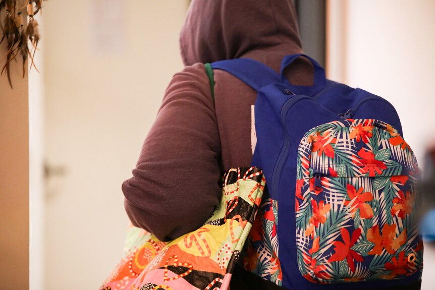 A shot of Kate from behind as she carries her backpack and other bags.