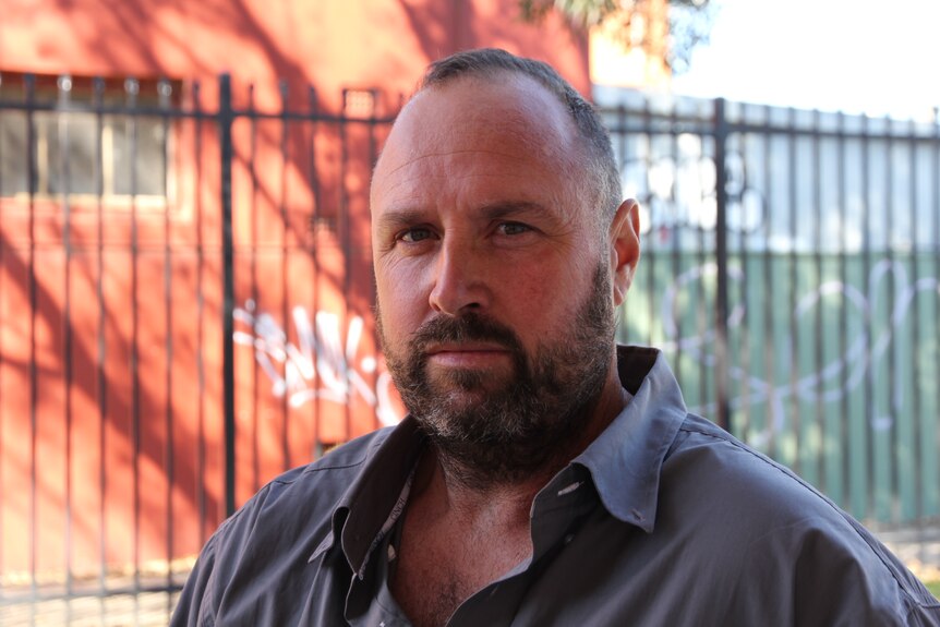 A man with a beard looking at the camera, serious, not smiling. 