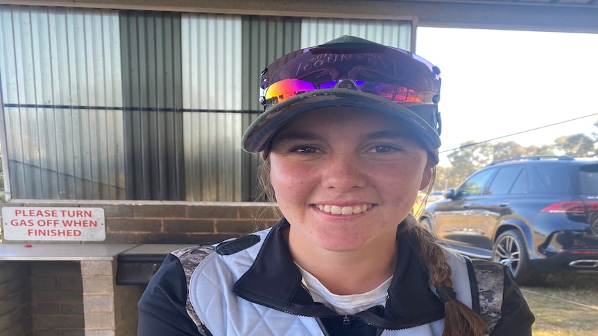 A young smiling girl with a plait over her shoulder, wearing a cap and blue and white shooting atire