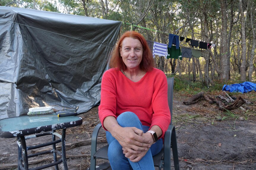 A woman with copper hair and a red jumper sits in from of a cloths line and grey tarp. 