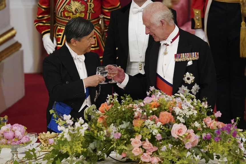 Emperor Naruhito and King Charles clink their glasses in front of a large bouquet of flowers