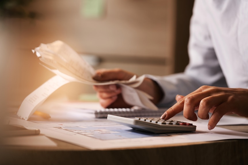 A person at a desk with a calculator and lots of receipts in their hand