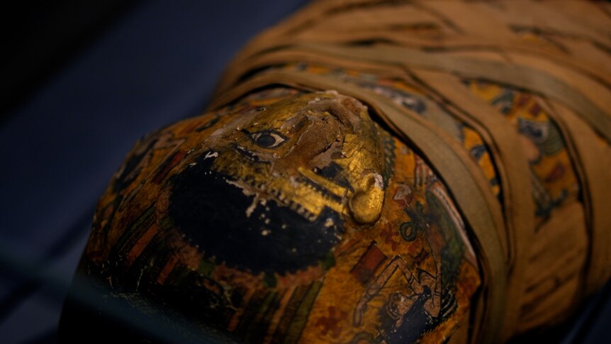 A closeup of the decorative, gold painted face covering on the mummified body of a boy 