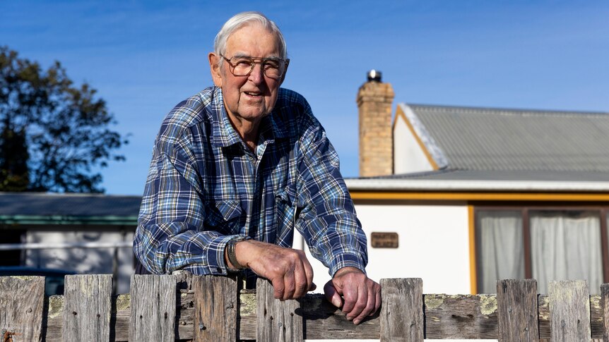 an elderly man leaning over a fence