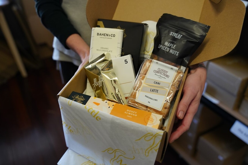 Women's hands holding a gift basket full of goodies.