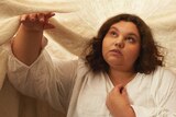 Kartanya Maynard is wearing a linen off-site shirt, posing under an off-white sheet.