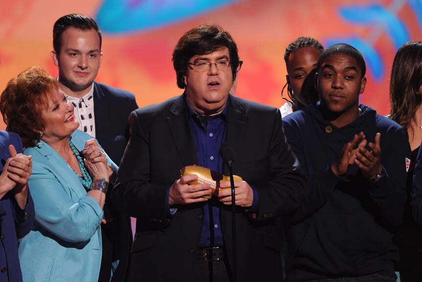 Nickelodeon producer Dan Schneider on stage with an award surrounded by people