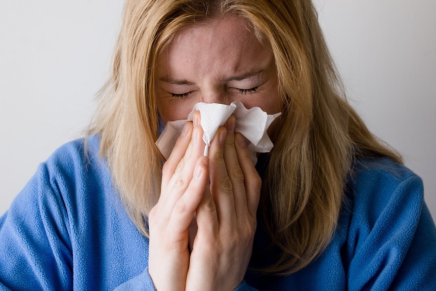 A woman in a blue top blowing her nose using a tissue