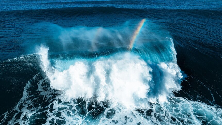 a huge wave crashes in the ocean with a rainbow in it