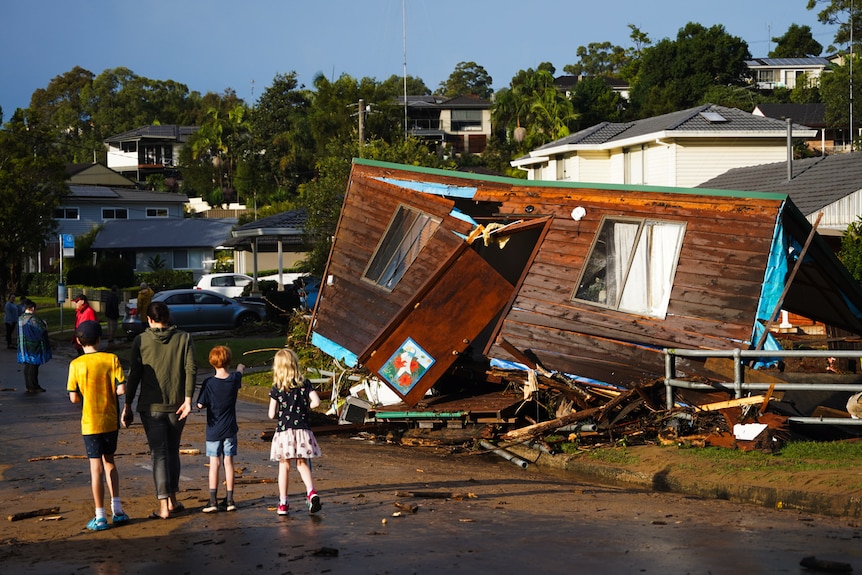 People walking past a brown clad granny flat washed onto side footpath.