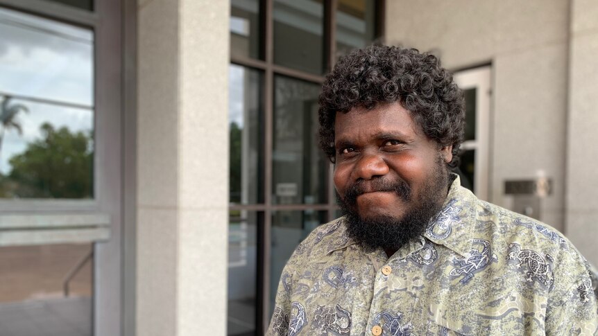 Indigenous man stands outside building and smiles 