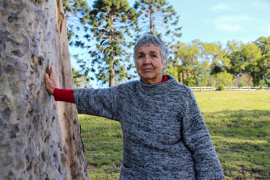 A leady leans against a big gum tree looking at the camera.