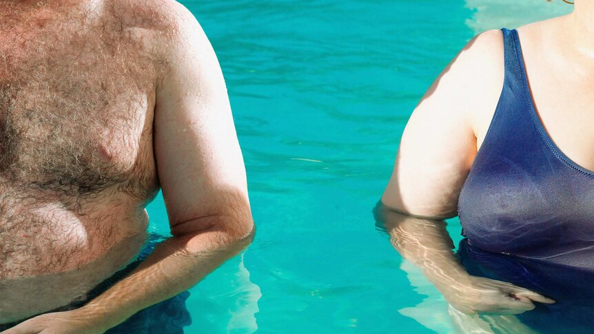 Unidentified overweight man and woman stand shoulder to shoulder in swimming pool.