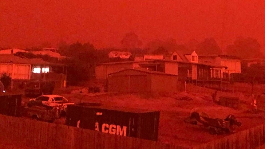 A bright red sky can be seen over houses.