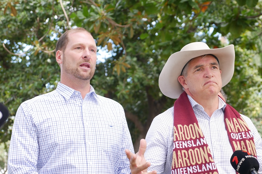 Two male politicians wearing light blue button downs. One wears a cowboy hat and a maroons scarf. 