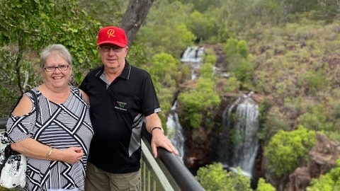 A woman in a black and white top and a man in a black top and red hat stand next to rail over looking a waterfall. 