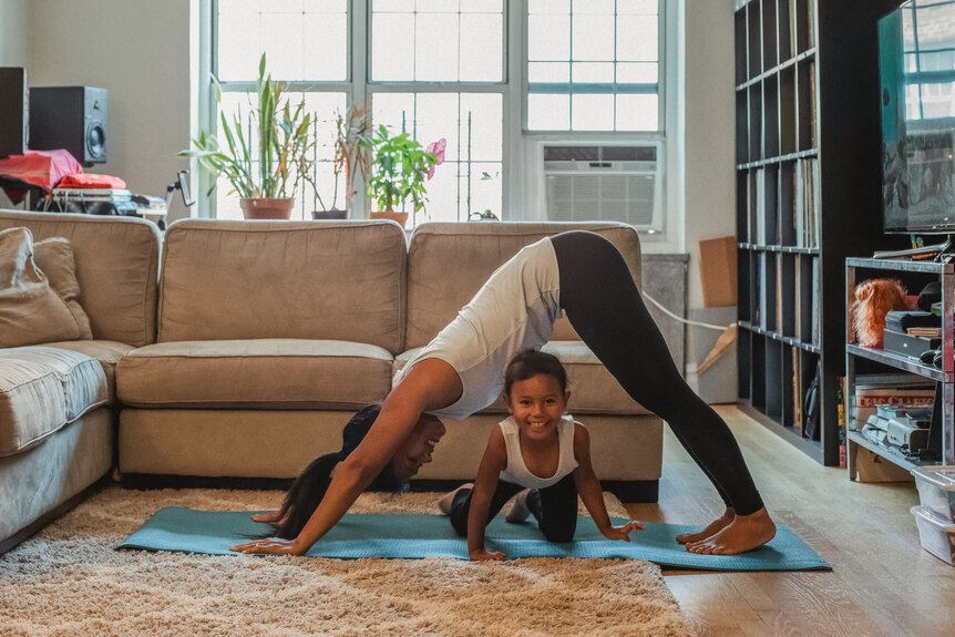 Mum doing downward dog yoga pose in lounge room with a young boy playing underneath her.