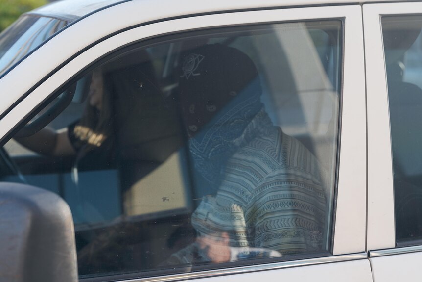 Man with bandana over face sits in passenger seat of car next to driver