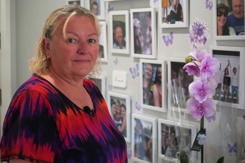 Woman staring at camera, in front of a picture frames on a wall 