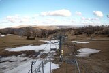 patches of snow on grass with ski lifts overhead