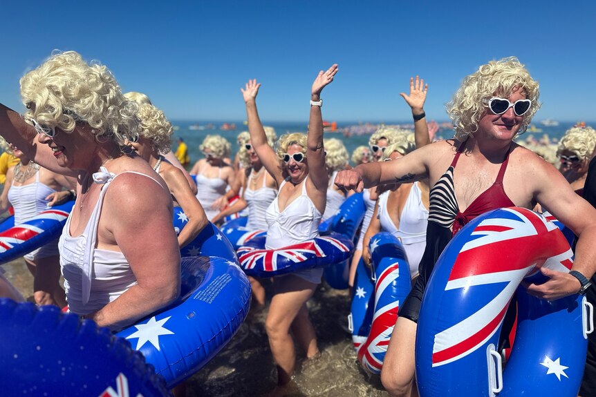 Swimmers with blue floaties and blonde wigs in the ocean.