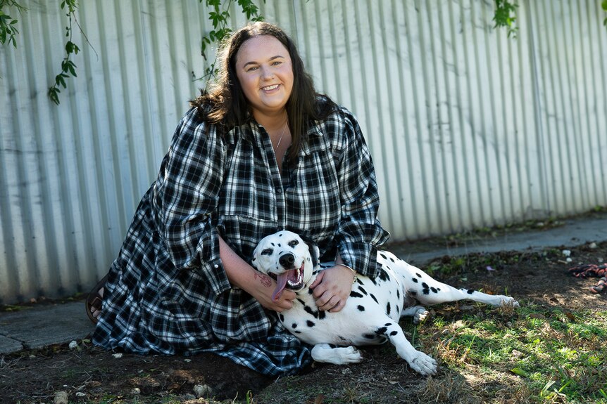 Woman and dog sit on grass and smile at camera in backyard