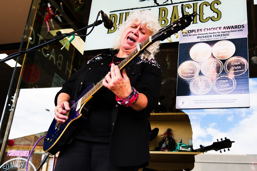 A woman sings and plays guitar in a street in a busking competition.