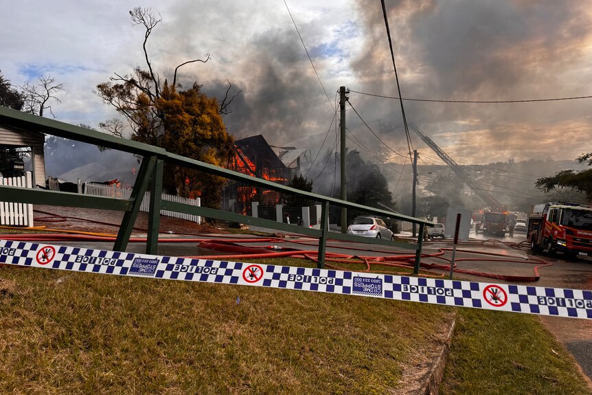 emergency crews on the street with a house ablaze behind them