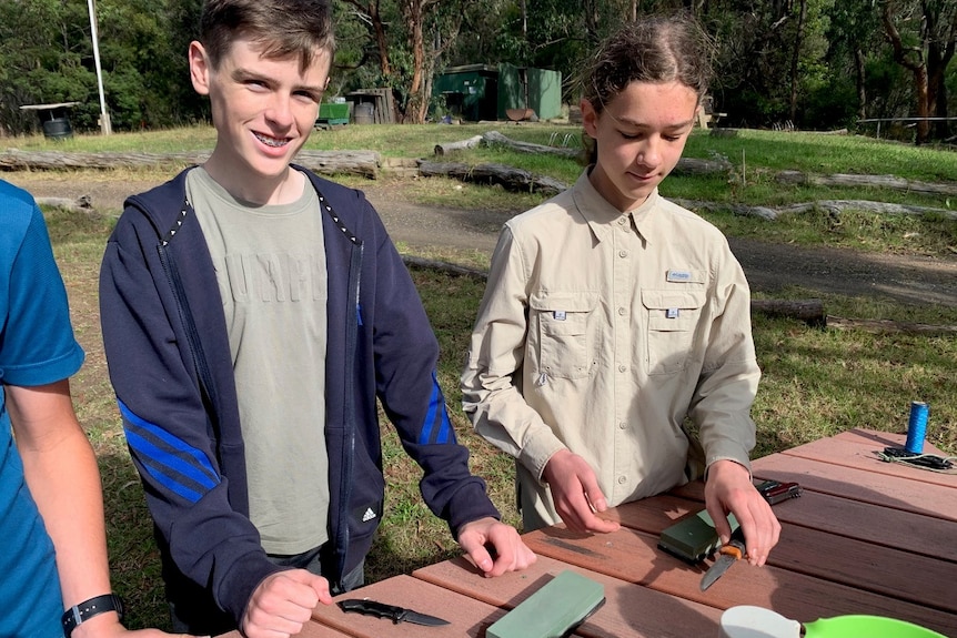 Two young children with knives and a sharpening stone